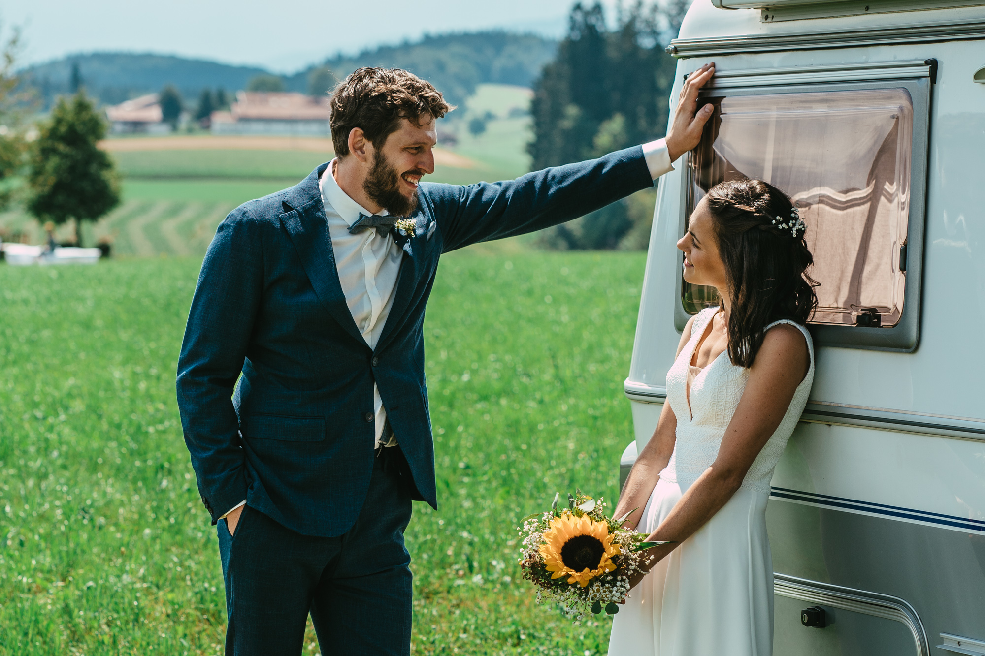 Lachender Mann mit Blüten im Haar wird von einer feiernden Gruppe umringt.